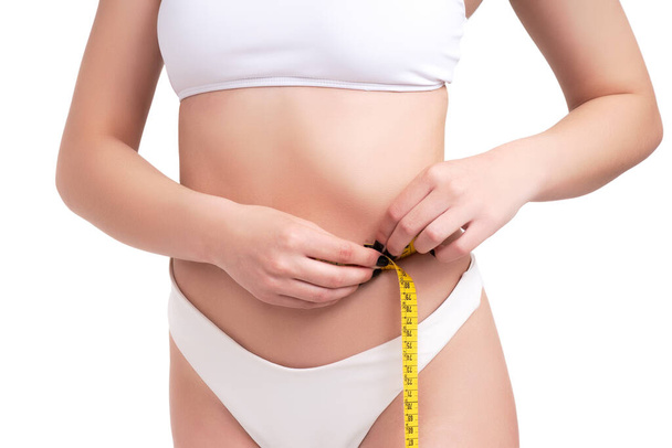 A closeup of a slim woman's torso measuring her thin waist in white underwear on a white background - Foto, imagen