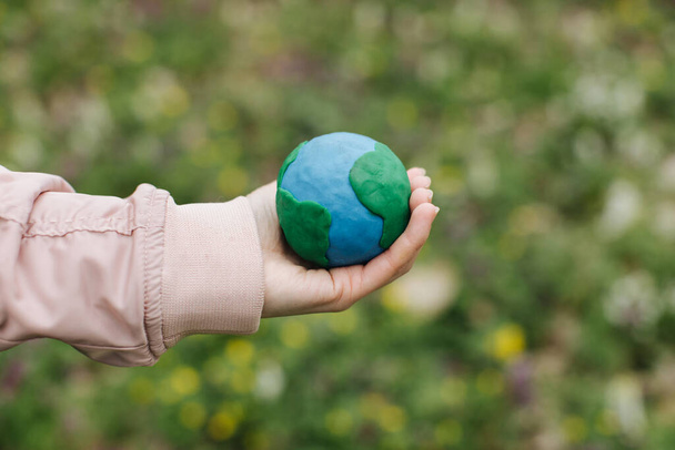 Female hands holding Earth in hands against green spring background. - Photo, Image