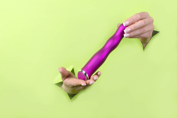 Female hands holding sex toys on a green background. Sex shop concept. - Photo, Image