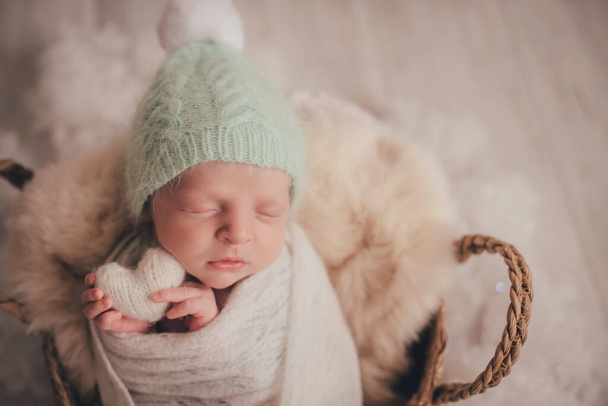 Um menino recém-nascido dorme e tem um coração de malha branca em suas alças. - Foto, Imagem