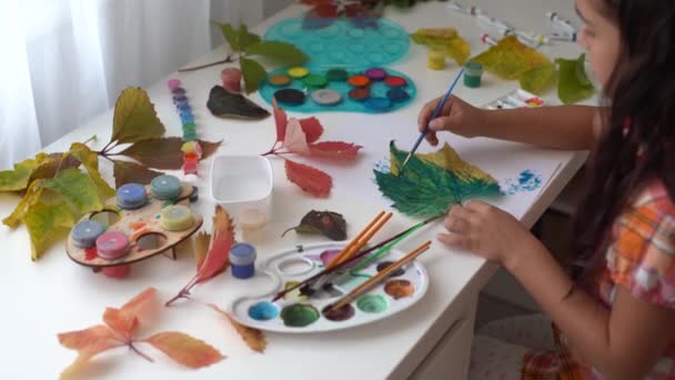 Petite fille peignant sur des feuilles jaunes d'automne avec gouache, arts pour enfants, créativité des enfants, art d'automne. - Séquence, vidéo