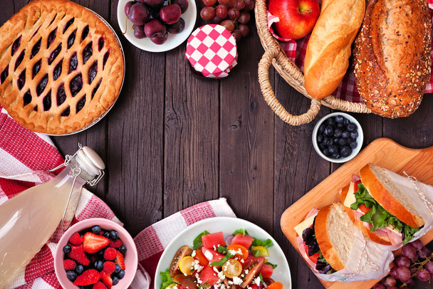 Summer picnic food frame. Overhead view on a wood background. Variety of cold salads, sandwiches, fruit and treats. Copy space. - Fotó, kép