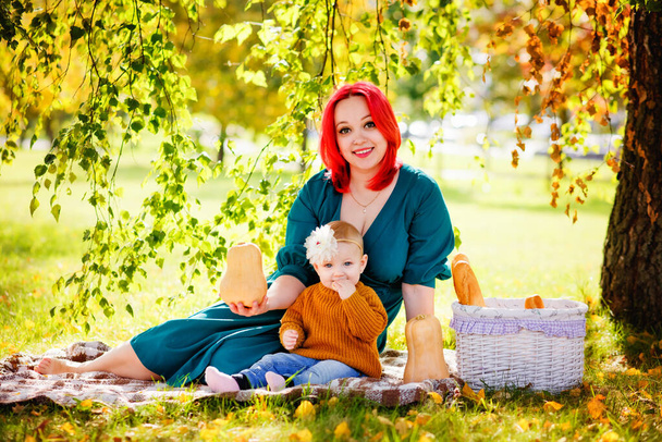 Una madre dai capelli rossi abbraccia la figlia, seduta su una coperta nel parco a fare un picnic al tramonto. Il concetto di vacanza estiva. Festa della mamma, la festa del bambino. Passate del tempo insieme. Luce del sole. - Foto, immagini