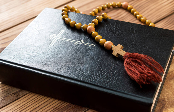Holy Bible with rosary beads on the wooden table.  - Foto, afbeelding