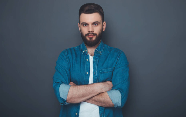 Confident serious hipster modern bearded man in jeans shirt with crossed arms is posing and looking right on the camera. - Photo, image