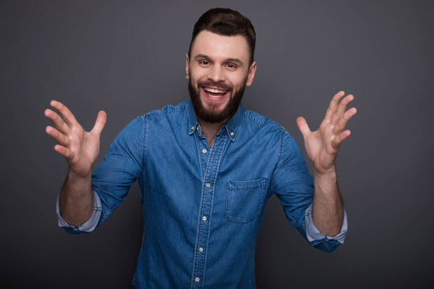 Excited smiling bearded man in jeans shirt is shouting, celebrating and having fun due to win - Фото, изображение