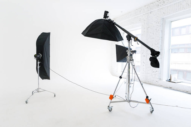 Empty photo studio with lighting equipment. Photographer workplace interior with professional tool set gear. Flash light, white background scenes ready for studio shooting. Modern photographer studio - Photo, Image