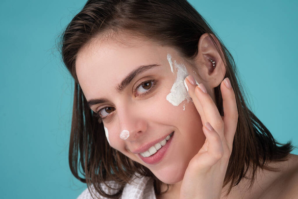 Beautiful young woman with clean fresh skin applying moisturizer cream on her pretty face. - Фото, зображення