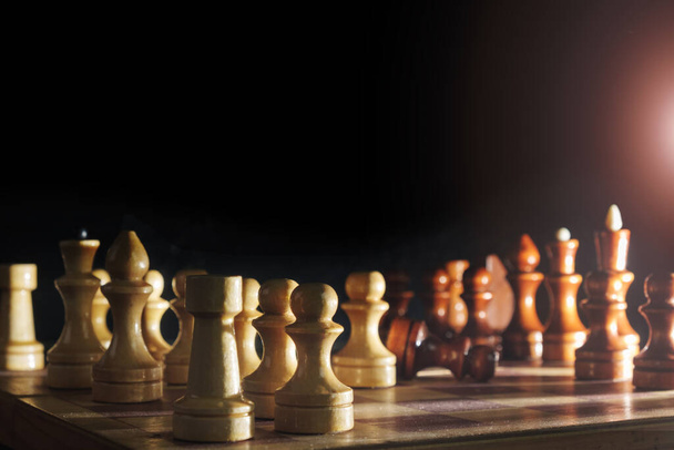 Piezas de ajedrez de madera y un tablero de ajedrez sobre fondo oscuro borroso, enfoque selectivo - Foto, Imagen