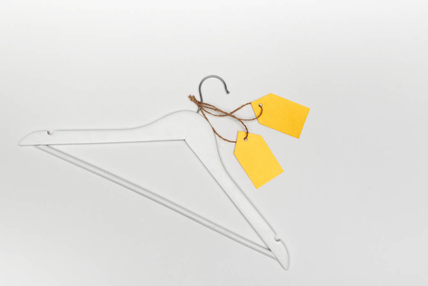 Kleiderbügel aus Holz mit gelben Papieretiketten auf weißem Hintergrund. Beschriften Sie leere Attrappen-Vorlage. Bekleidungsmarke. - Foto, Bild