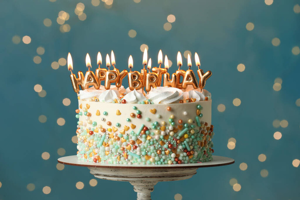 Beautiful birthday cake with burning candles on stand against festive lights - Foto, Imagen