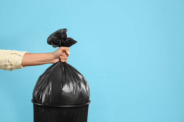 Woman taking garbage bag out of bin on light blue background, closeup. Space for text - Photo, image