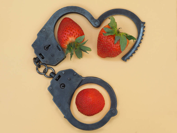 Police handcuffs and strawberries on a yellow table background. The concept of sexual and intimate innuendo or flirtation. Bright photo for advertising adult toys or entertainment. - Photo, Image
