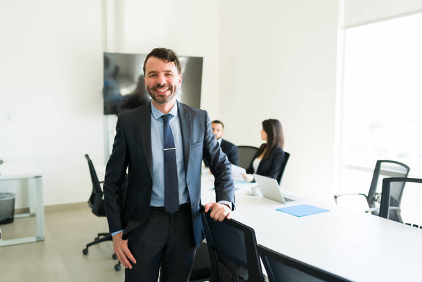 Representante de vendas hispânico feliz em um terno sorrindo e se sentindo feliz depois de fazer um acordo de vendas bem sucedido com executivos de negócios na sala de reuniões - Foto, Imagem