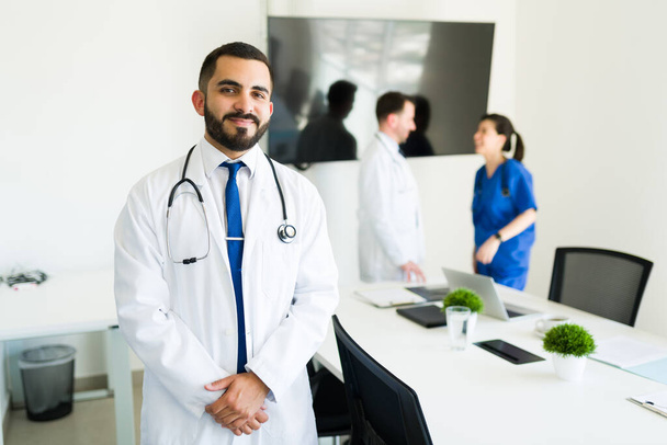 Рад помочь своим пациентам. Успешный латиноамериканец и директор больницы в белом халате готовятся начать встречу с медицинским советом - Фото, изображение