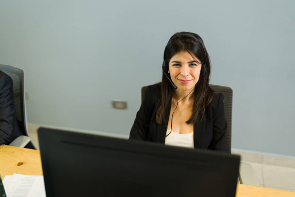 Portret van een hardwerkende jonge vrouw die wacht op telefoontjes van klanten in een callcenter. Gelukkige vertegenwoordiger doet telemarketing en glimlachen - Foto, afbeelding