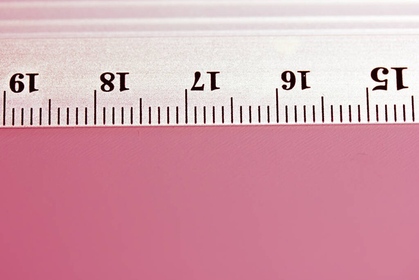 Металлическая линейка крупным планом на розовом фоне. Верхний вид простой линейки с сантиметрами, миллиметрами, единицами измерения длины индикаторов. Оборудование для учебы. Инструменты для школьников, студентов. - Фото, изображение