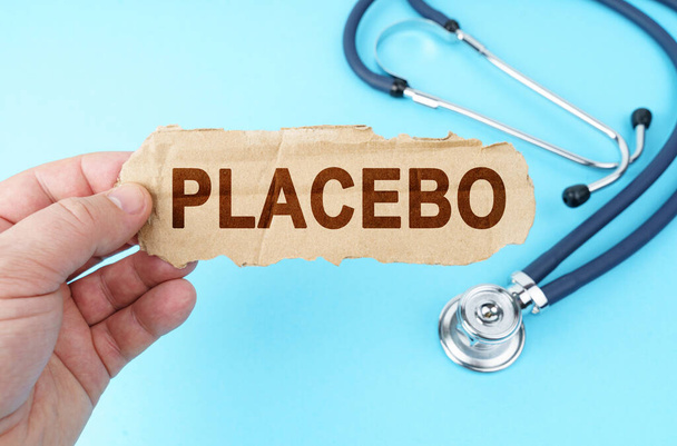 Medicine and health concept. On a blue background, a man holds a cardboard box with the inscription - PLACEBO - Foto, Imagen