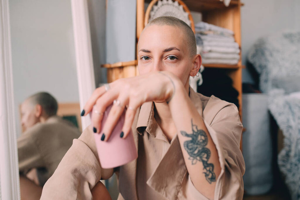 Donna con i capelli corti seduta a terra e in possesso di tazza con bevanda - Foto, immagini