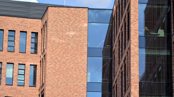 Σύγχρονη τούβλο και γυάλινη πρόσοψη του κτιρίου γραφείων. Ένας αντιφατικός συνδυασμός υφής ουρανού και τούβλων σε ένα κτίριο. Αρχιτεκτονική πρόσοψη κτιρίου με κόκκινα τούβλα.. - Φωτογραφία, εικόνα