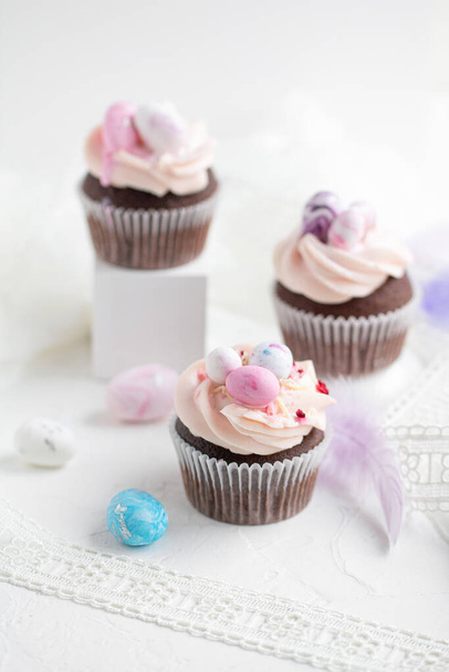Three Easter chocolate cupcakes with caramel filling and decoration of small Easter eggs from marzipan on the white background. Selective focus - Фото, зображення
