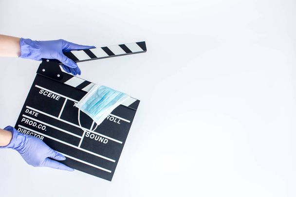Nainen sinisissä kertakäyttöisissä kumihanskoissa pitelemässä elokuvataputtajaa. Pandemian vaikutus elokuvateattereihin - Valokuva, kuva