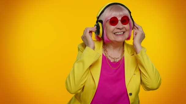 Starsza kobieta słuchająca muzyki na słuchawkach tańcząca disco oszukując, bawiąc się, gestykulując dłońmi - Materiał filmowy, wideo