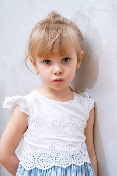 mała dziewczynka w lekkiej eleganckiej sukience stoi pod ścianą w pokoju - Zdjęcie, obraz