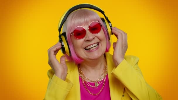 Yaşlı kadın kulaklıkla müzik dinliyor, disko dansı yapıyor, eğleniyor, el kol hareketi yapıyor. - Video, Çekim