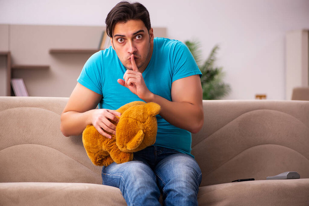 Jeune homme assis avec jouet ours à la maison - Photo, image