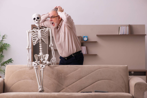 Alter Mann sitzt auf dem Sofa mit dem weiblichen Skelett - Foto, Bild