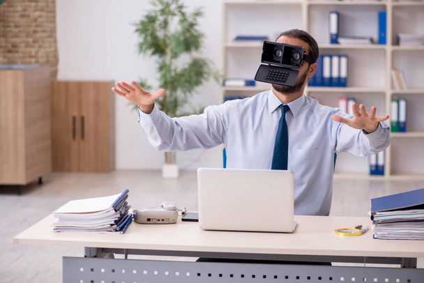 Jonge mannelijke werknemer met een virtuele bril op de werkplek - Foto, afbeelding