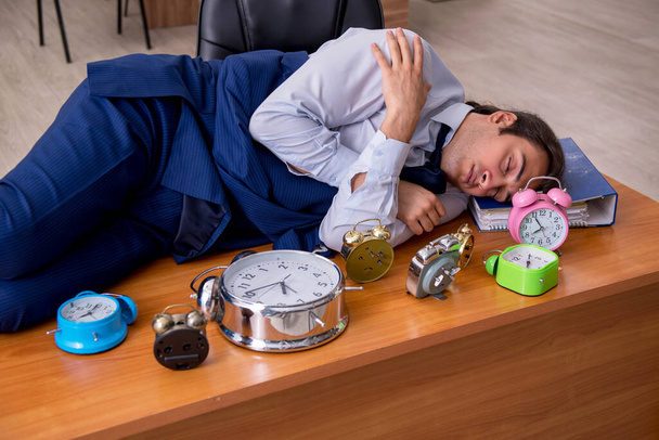 Νεαρός άνδρας εργαζόμενος κοιμάται στο γραφείο στη διαχείριση του χρόνου - Φωτογραφία, εικόνα