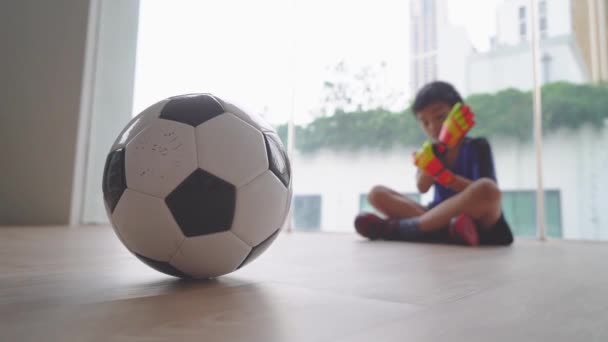 Little soccer boy is getting ready for practicing Objetivo manter em casa em uma sala com bola de futebol em primeiro plano. - Filmagem, Vídeo