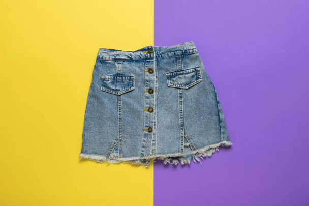 Short denim skirt on a background of yellow and purple flowers. Summer denim clothing. - Photo, Image