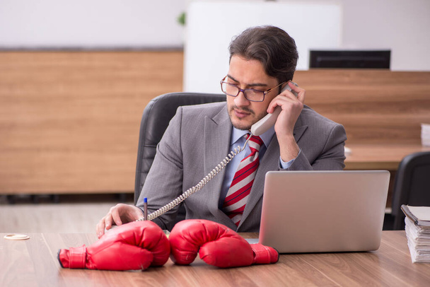 Young male employee wearing boxing gloves at workplace - Photo, Image