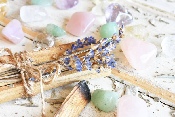 Een close-up van Palo Santo wierookstokjes met gedroogde lavendel en helende kristallen op een witte achtergrond.  - Foto, afbeelding