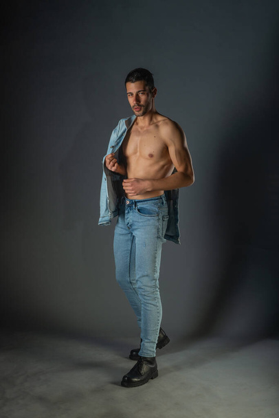 Full body portrait of sports man with denim jeans posing with bare torso in a dark studio - Fotoğraf, Görsel