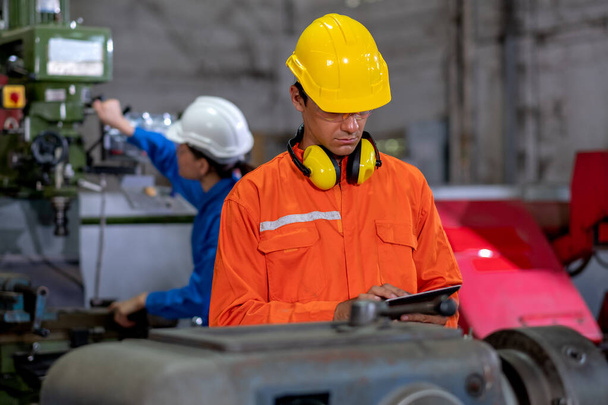 Factory worker man hold tablet and inspect the function while her co-worker work with other machine in the background. Maintenance and check system support industrial business. - Photo, image