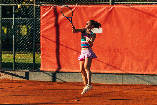 Καυκάσια γυναίκα με σπορ στολή που παίζει τένις σε πήλινο γήπεδο - Φωτογραφία, εικόνα