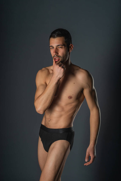Retrato de primer plano de moda de un guapo macho con torso desnudo posando en ropa interior negra sobre un fondo aislado - Foto, imagen