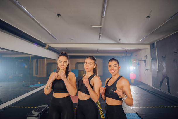 Портрет трех сильных женщин в спортивной одежде, позирующих в спортзале - Фото, изображение