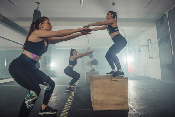 Skupina atletických mladých fit dívky ve sportovním oblečení dělá dřepy, mají intenzivní nohy cvičení - Fotografie, Obrázek