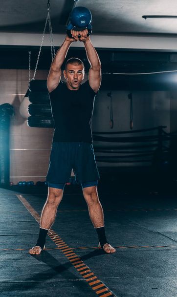 Спортсмен тренується в спортзалі, він робить важку атлетику з чайником
 - Фото, зображення