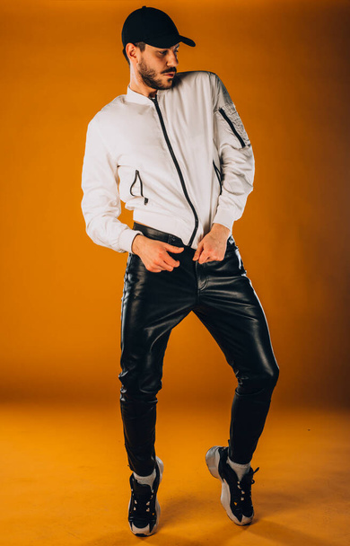 Στιγμιότυπο ενός μοντέρνου νεαρού άνδρα με μοντέρνο λευκό μπουφάν και δερμάτινο παντελόνι - Φωτογραφία, εικόνα