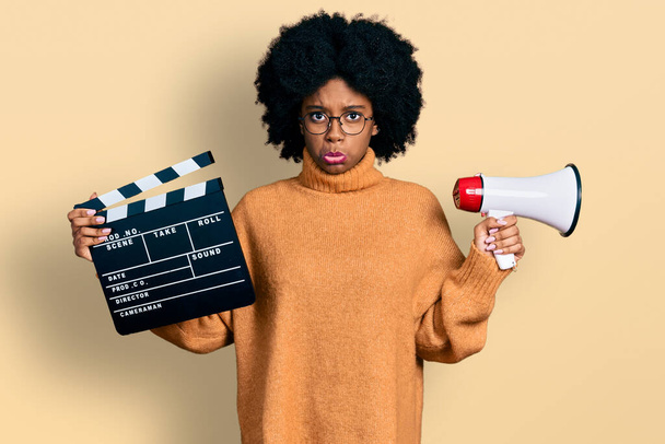 Young african american woman holding video film clapboard and megaphone depressed and worry for distress, crying angry and afraid. sad expression.  - Photo, Image
