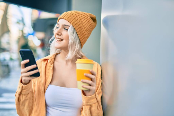 Junge Blondine nutzt Smartphone und trinkt Kaffee in der Stadt. - Foto, Bild
