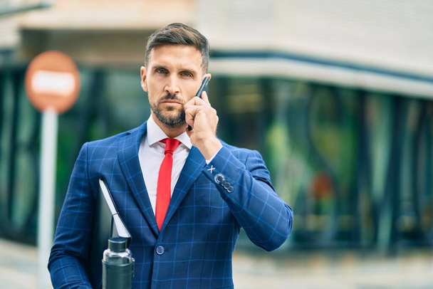 Junger kaukasischer Geschäftsmann mit ernstem Gesichtsausdruck spricht auf dem Smartphone in der Stadt. - Foto, Bild