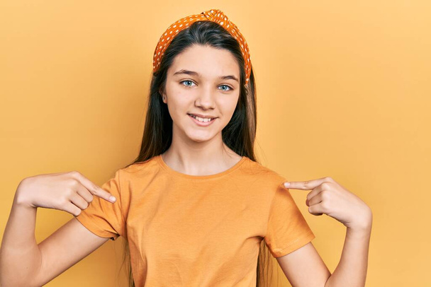 Fiatal barna lány visel alkalmi narancs póló néz magabiztos mosollyal az arcon, rámutatva önmagára ujjaival büszke és boldog.  - Fotó, kép