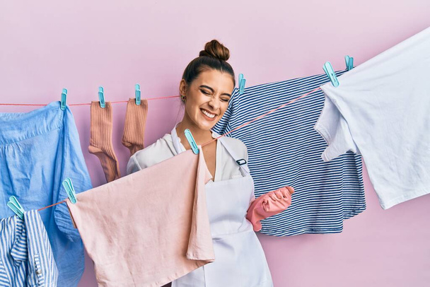 Beautiful brunette young woman washing clothes at clothesline excited for success with arms raised and eyes closed celebrating victory smiling. winner concept.  - Photo, Image